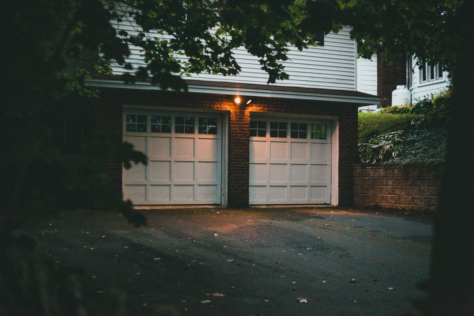 Two white residential garage doors at dusk with a warm porch light